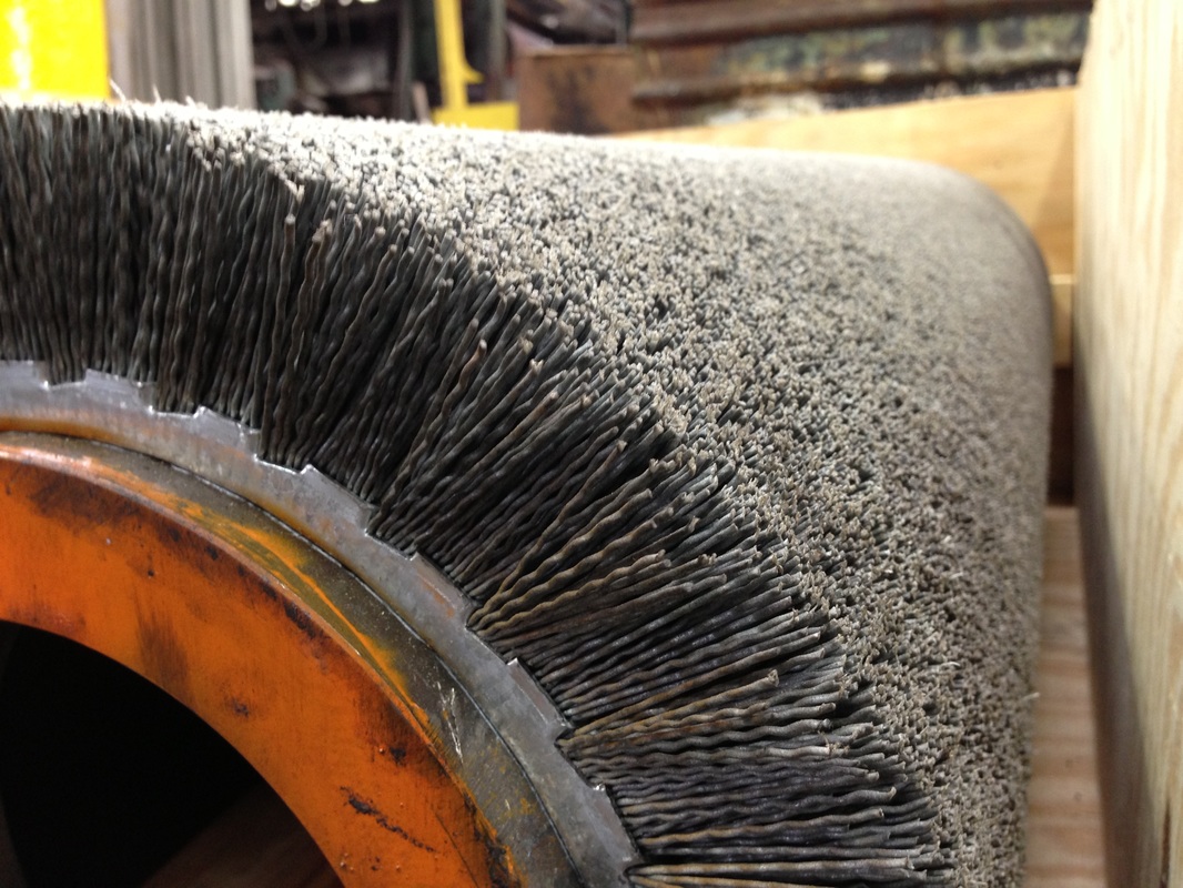 Picturepicture of two wide face abrasive bristle brush tubes for cleaning and finishing metal strip in a crate